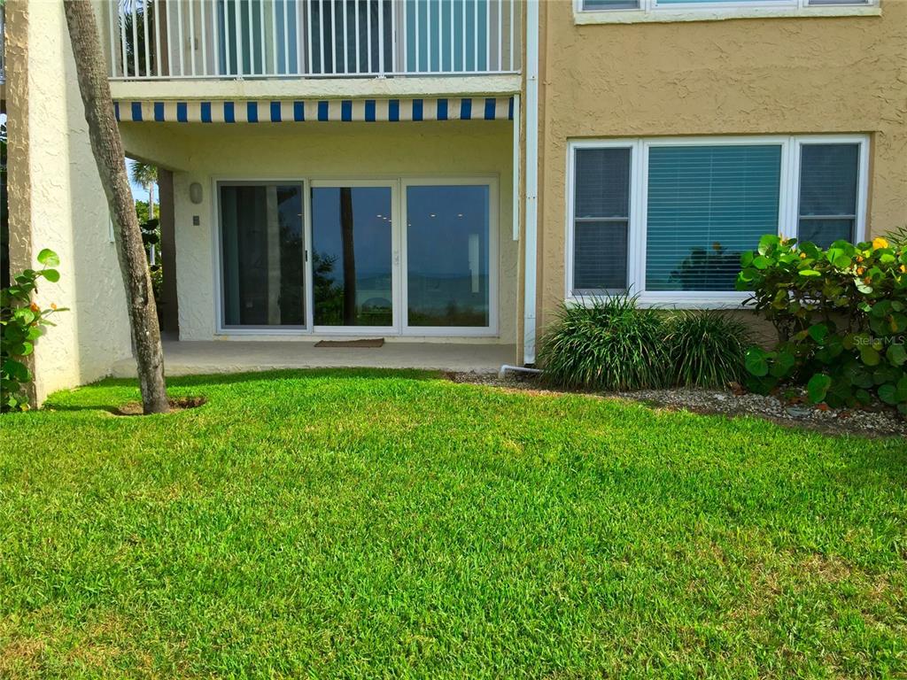 A ground-level patio with sliding glass doors sits beside a grassy lawn and landscaping — 3400 GULF BOULEVARD UNIT 108, BELLEAIR BEACH, FL