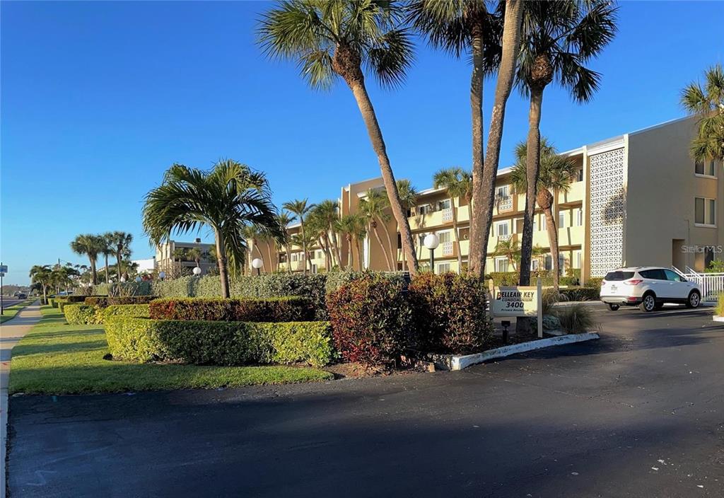 A multi-story condominium building stands behind a landscaped lawn with palm trees and parking — 3400 GULF BOULEVARD UNIT 108, BELLEAIR BEACH, FL
