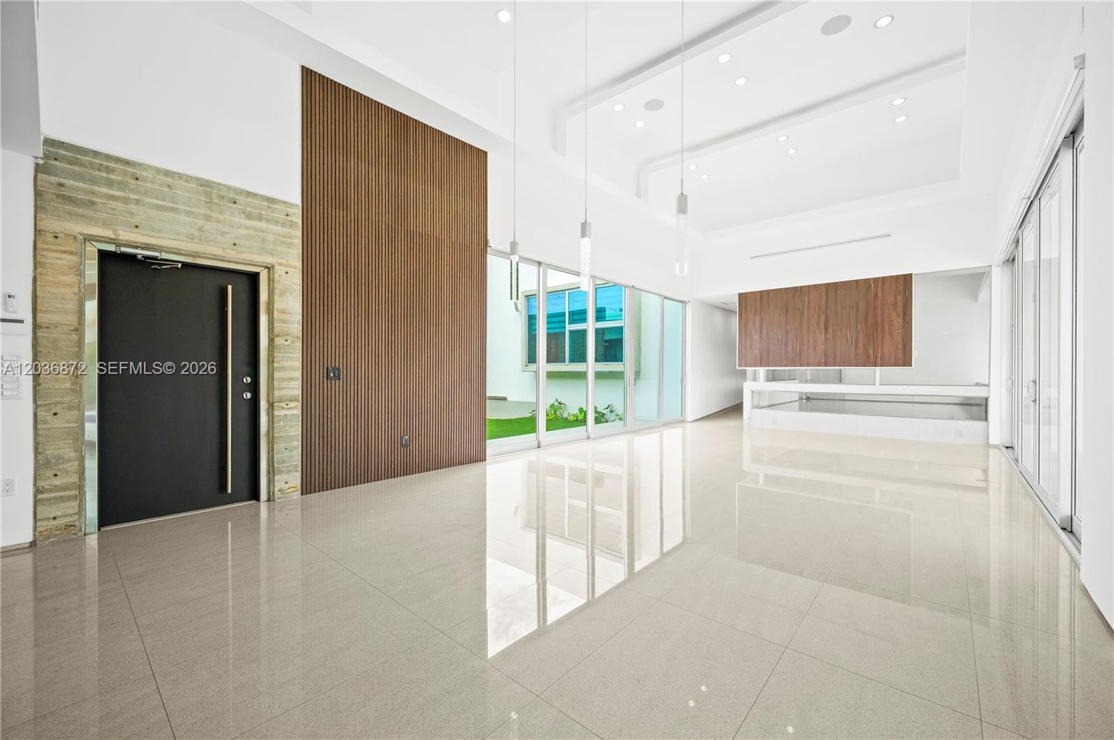 A modern, high-ceilinged room features large floor tiles, a wood-slat wall, and glass sliding doors — 2360 SW 139th Ave, Miami FL 33175, MIAMI, FL