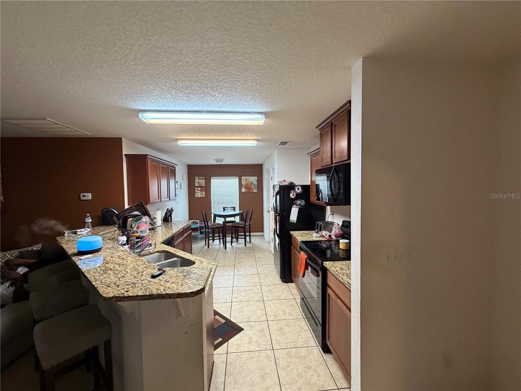 A kitchen features granite countertops, dark wood cabinets, black appliances, and a dining area beyond — 487 OCHO RIOS AVENUE, TAVARES, FL