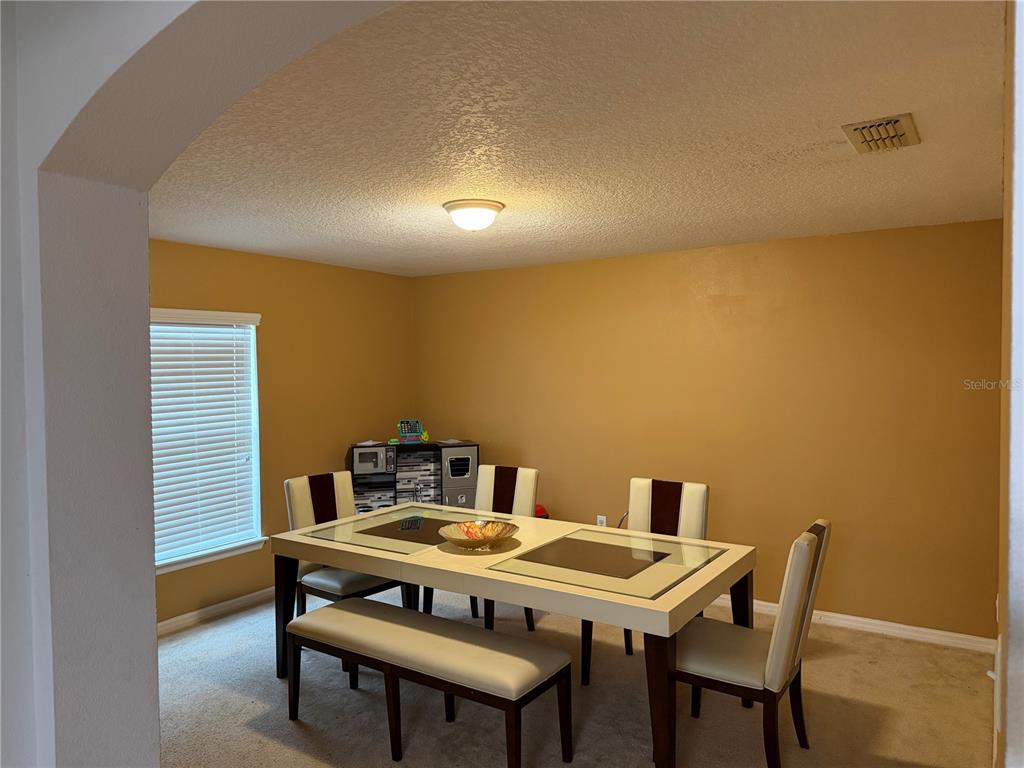 A dining room features a glass-topped table, four chairs, a bench, and tan walls — 487 OCHO RIOS AVENUE, TAVARES, FL