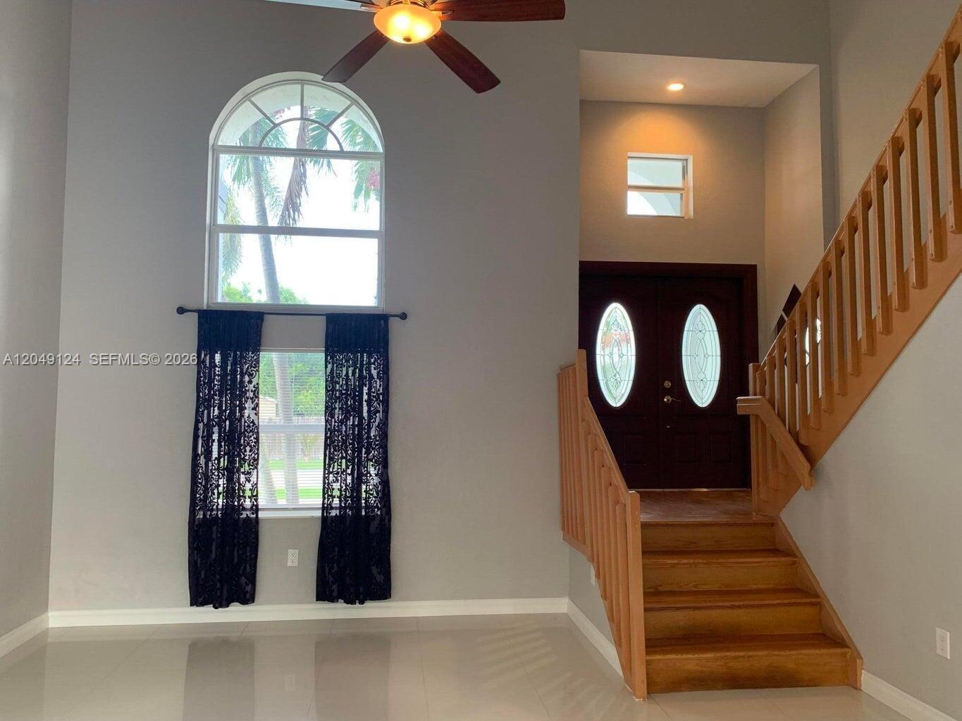A high-ceilinged foyer features a wooden staircase, tile flooring, and a large arched window — 12948 NW 10th St, Miami FL 33182, MIAMI, FL