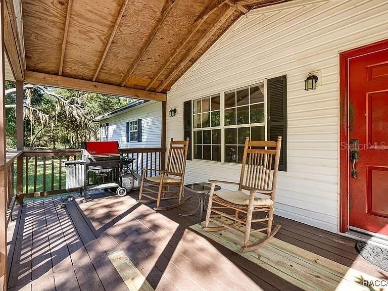 A wooden porch features two rocking chairs, a small table, and a grill — 8171 SE 144TH PLACE, INGLIS, FL