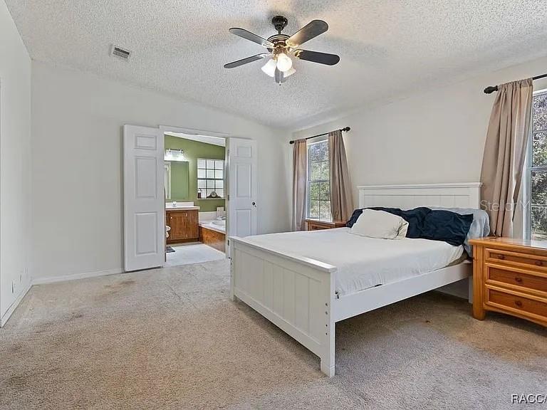A bedroom features a white bed, beige carpet, a ceiling fan, and an attached bathroom — 8171 SE 144TH PLACE, INGLIS, FL