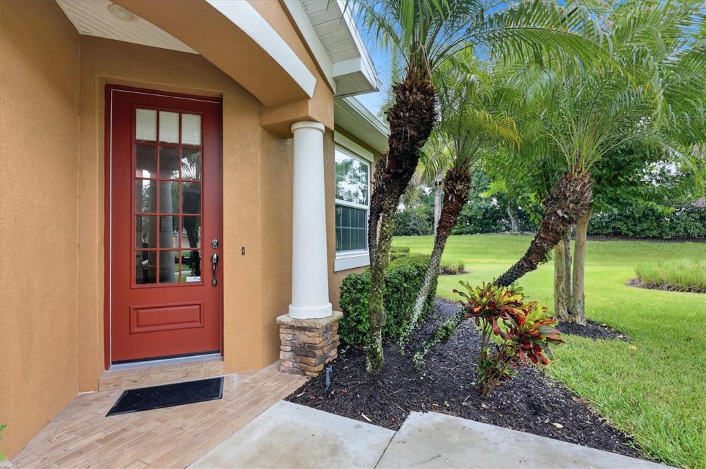 A red front door with a glass pane sits next to a white column and palms — 11447 52ND COURT E, PARRISH, FL