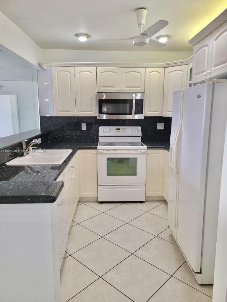 A kitchen features white cabinets, black countertops, white appliances, and light-colored tiled flooring — 600 Three Islands Blvd # 1817, Hallandale Beach FL 33009, HALLANDALE BEACH, FL