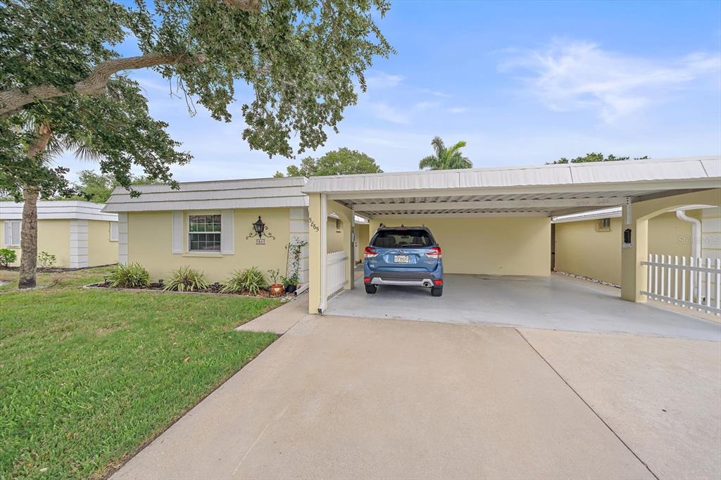 A yellow single-story house features a concrete driveway and a covered carport with a car — 5865 TIDEWOOD AVENUE UNIT 8, SARASOTA, FL