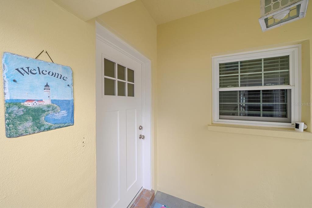 A white front door with a lighthouse welcome sign sits beside a window — 5865 TIDEWOOD AVENUE UNIT 8, SARASOTA, FL