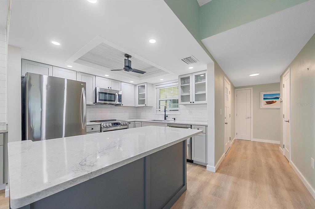A kitchen features a large island, stainless steel appliances, white cabinets, and light wood flooring — 5865 TIDEWOOD AVENUE UNIT 8, SARASOTA, FL