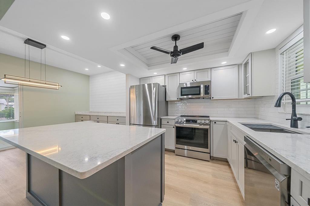 A modern kitchen features a central island, white cabinetry, stainless steel appliances, and a ceiling fan — 5865 TIDEWOOD AVENUE UNIT 8, SARASOTA, FL