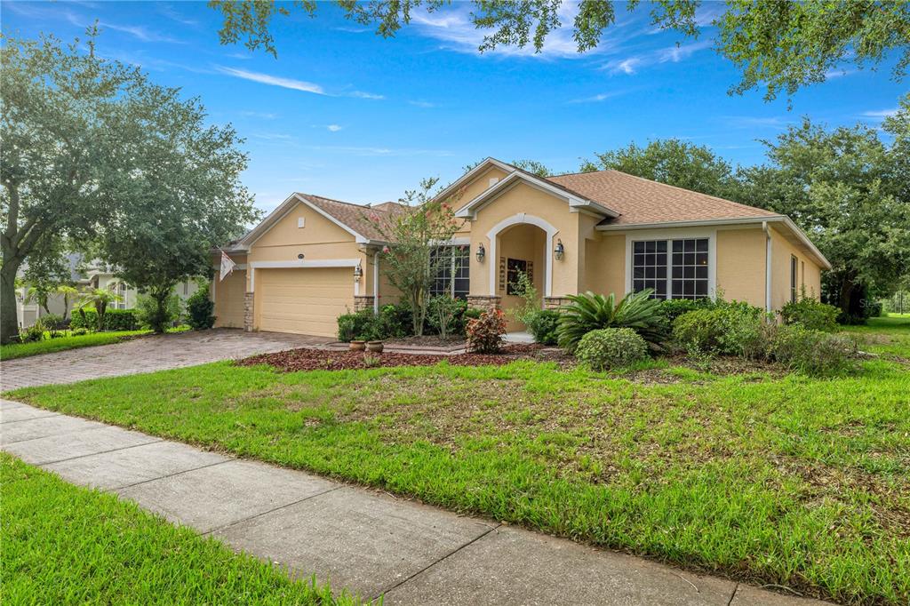 A single-story tan stucco house with a two-car garage and a landscaped front yard — 1271 LATTIMORE DRIVE, CLERMONT, FL