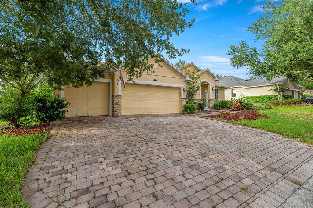 A single-story house with a paved driveway, a three-car garage, and mature trees — 1271 LATTIMORE DRIVE, CLERMONT, FL