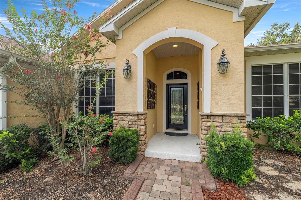 The exterior of a house features a stone-accented entryway with a black glass-paneled front door — 1271 LATTIMORE DRIVE, CLERMONT, FL