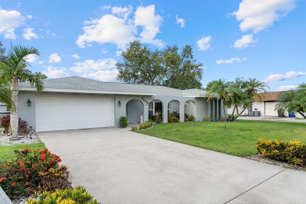 A single-story gray house with a two-car garage and arched entryway sits on a lawn — 5206 18TH AVENUE E, BRADENTON, FL