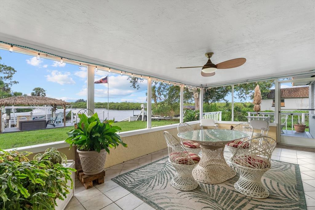 A screened-in patio features a glass dining table, white wicker chairs, and a waterfront view — 5206 18TH AVENUE E, BRADENTON, FL