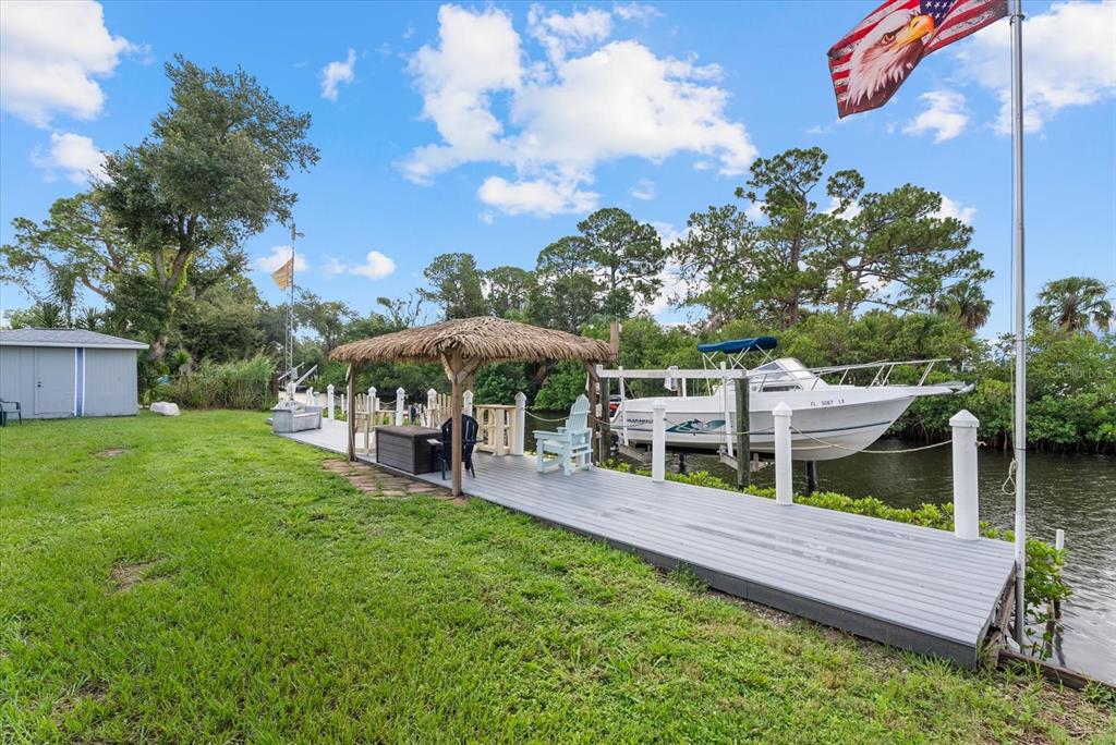 A wooden dock with a tiki-style roof sits beside a boat on a grassy waterfront — 5206 18TH AVENUE E, BRADENTON, FL