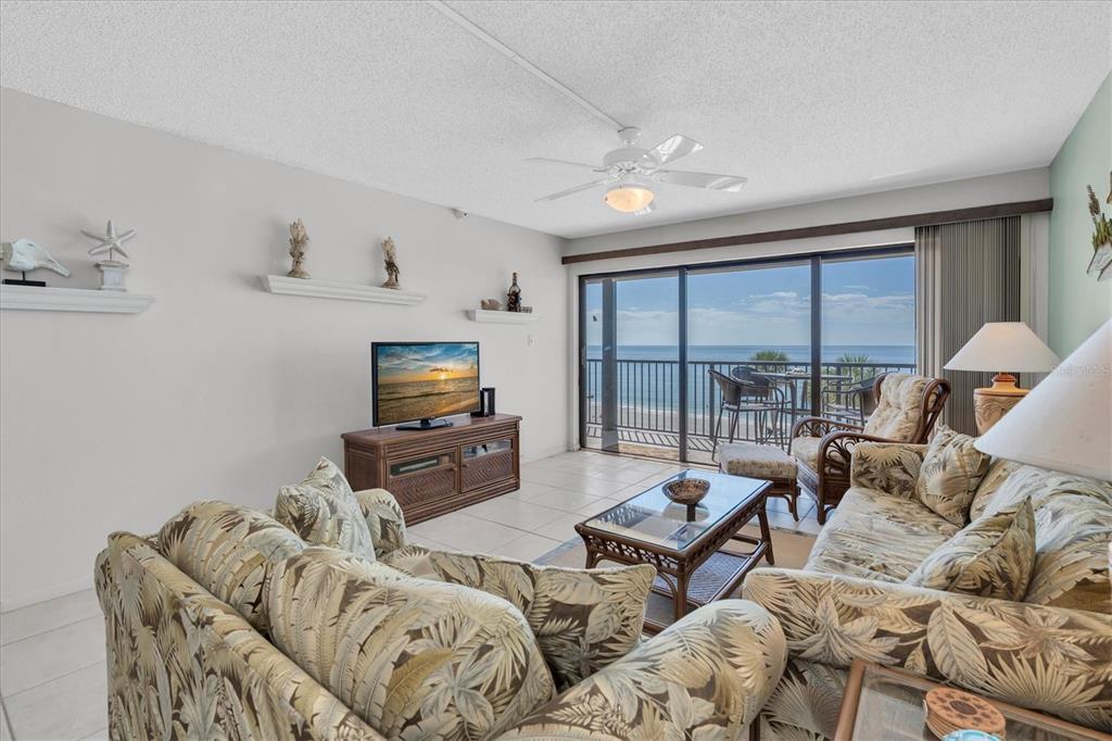 A living room with tropical-print furniture, a television, and a balcony overlooking the ocean — 14950 GULF BOULEVARD UNIT 402, MADEIRA BEACH, FL