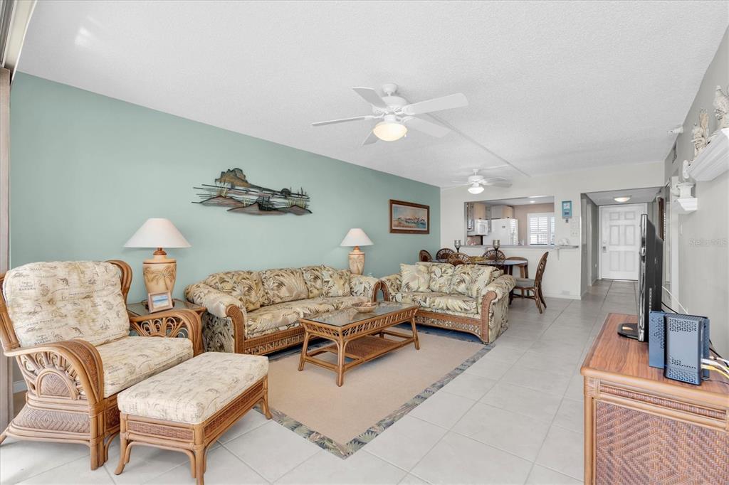 A living room features wicker furniture, a light blue accent wall, and tile flooring — 14950 GULF BOULEVARD UNIT 402, MADEIRA BEACH, FL