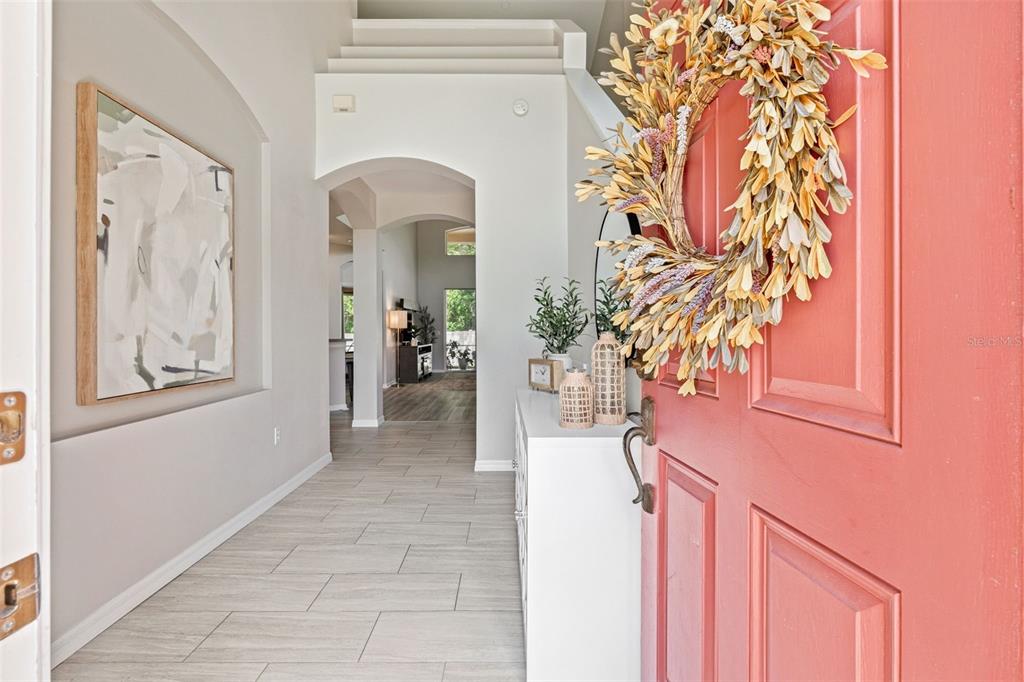 A view from an open coral-colored front door into a tiled entryway and hallway — 11809 ACORN WOODS TERRACE, LAKEWOOD RANCH, FL
