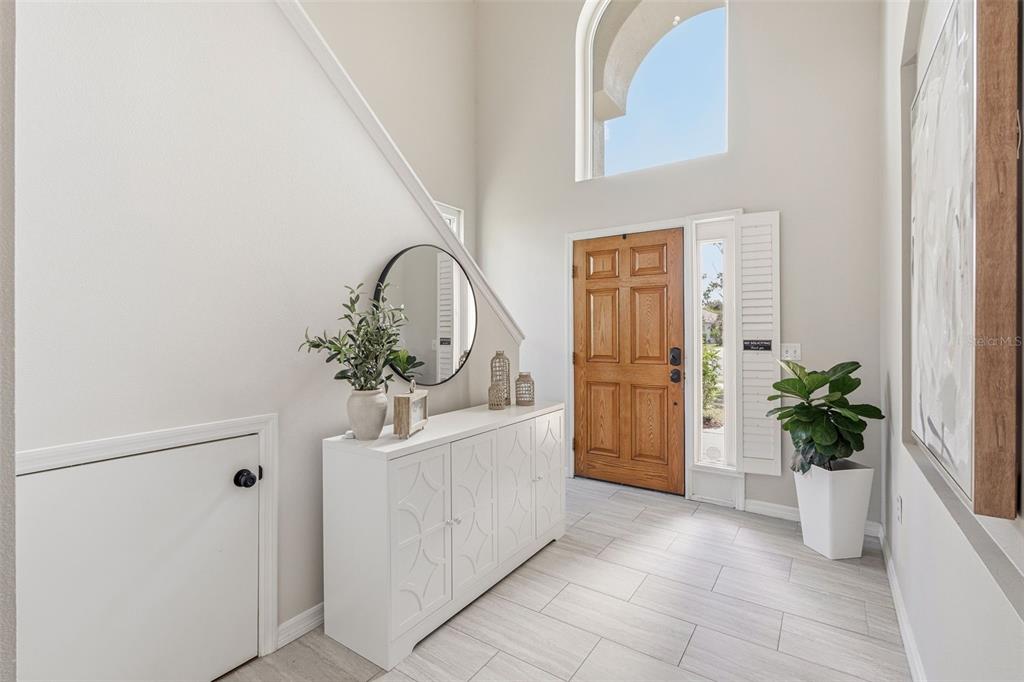 A bright entryway features a wooden front door, white console table, and light tile flooring — 11809 ACORN WOODS TERRACE, LAKEWOOD RANCH, FL