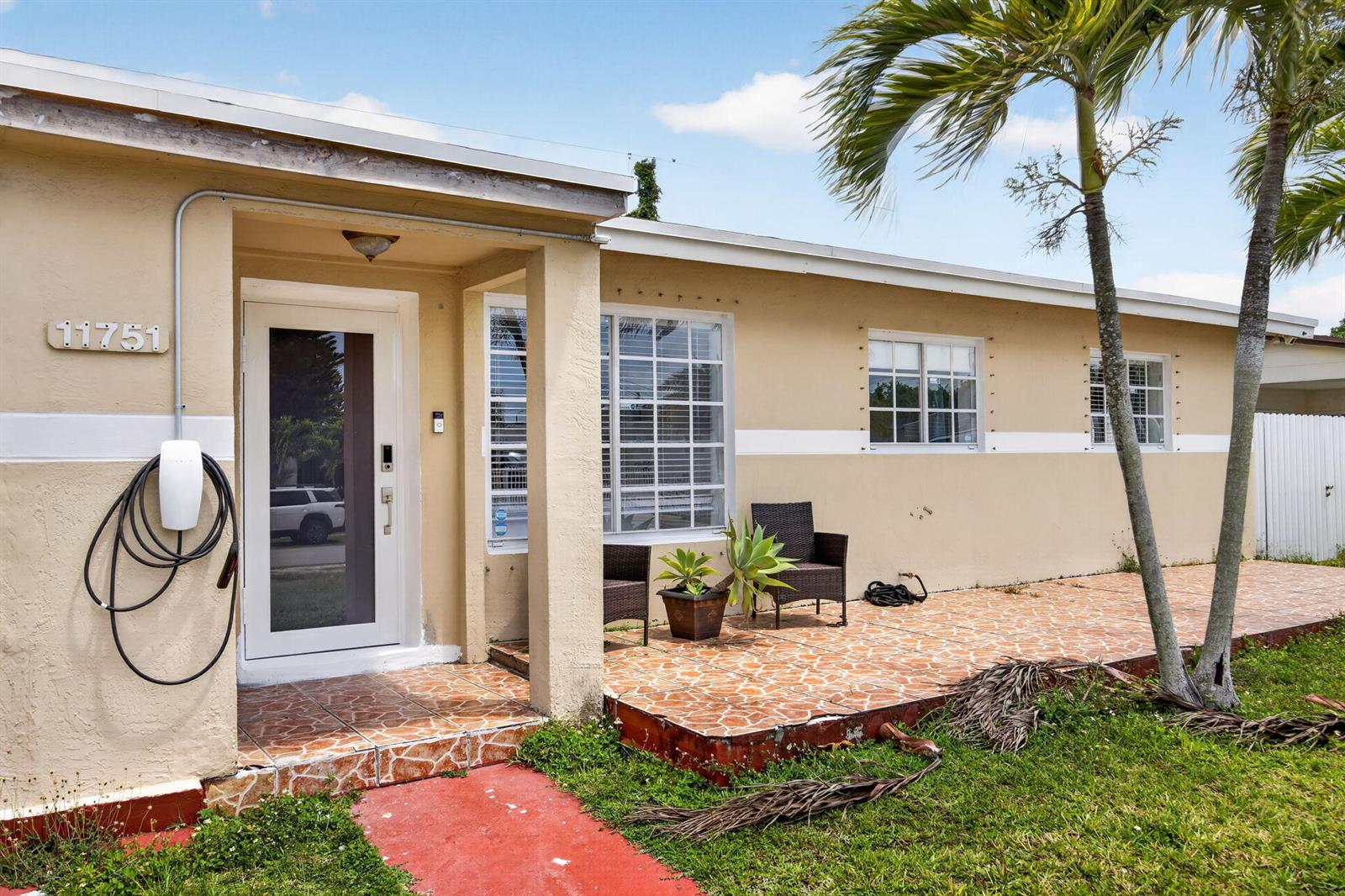 A single-story house exterior features a tiled patio, a front door, and an EV charger — 11751 SW 185th Terrace, Miami FL 33177, MIAMI, FL