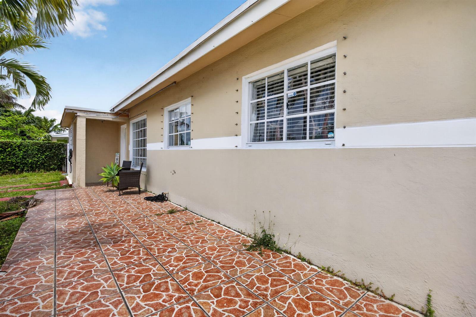 A tan exterior wall features two windows with hurricane shutter anchors and a tiled patio — 11751 SW 185th Terrace, Miami FL 33177, MIAMI, FL