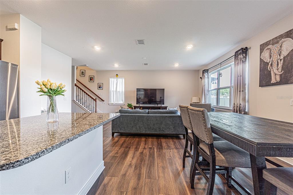 A kitchen island with granite countertops overlooks a dining area and a living room — 21027 MONZA LOOP, LAND O LAKES, FL
