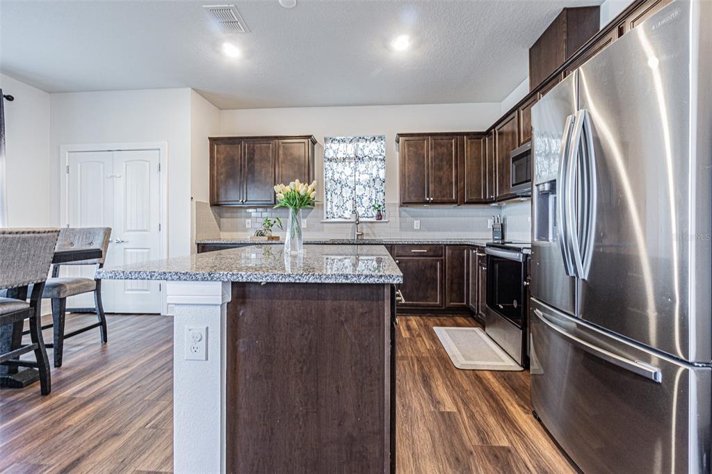 A kitchen features dark wood cabinets, granite countertops, a center island, and stainless steel appliances — 21027 MONZA LOOP, LAND O LAKES, FL