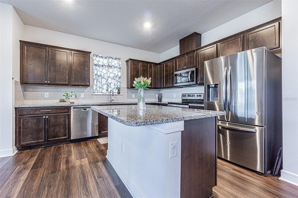 A kitchen with dark wood cabinets, granite countertops, stainless steel appliances, and wood-look flooring — 21027 MONZA LOOP, LAND O LAKES, FL