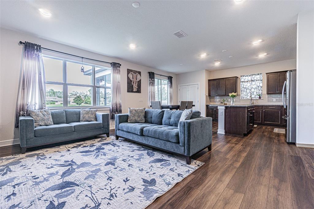 A living room with two blue sofas and a patterned rug opens to a kitchen — 21027 MONZA LOOP, LAND O LAKES, FL