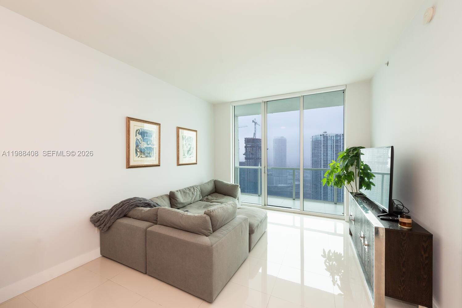 A living room features a grey sectional sofa, a television on a console, and floor-to-ceiling windows — 55 SE 6th St # 4200, Miami FL 33131, MIAMI, FL