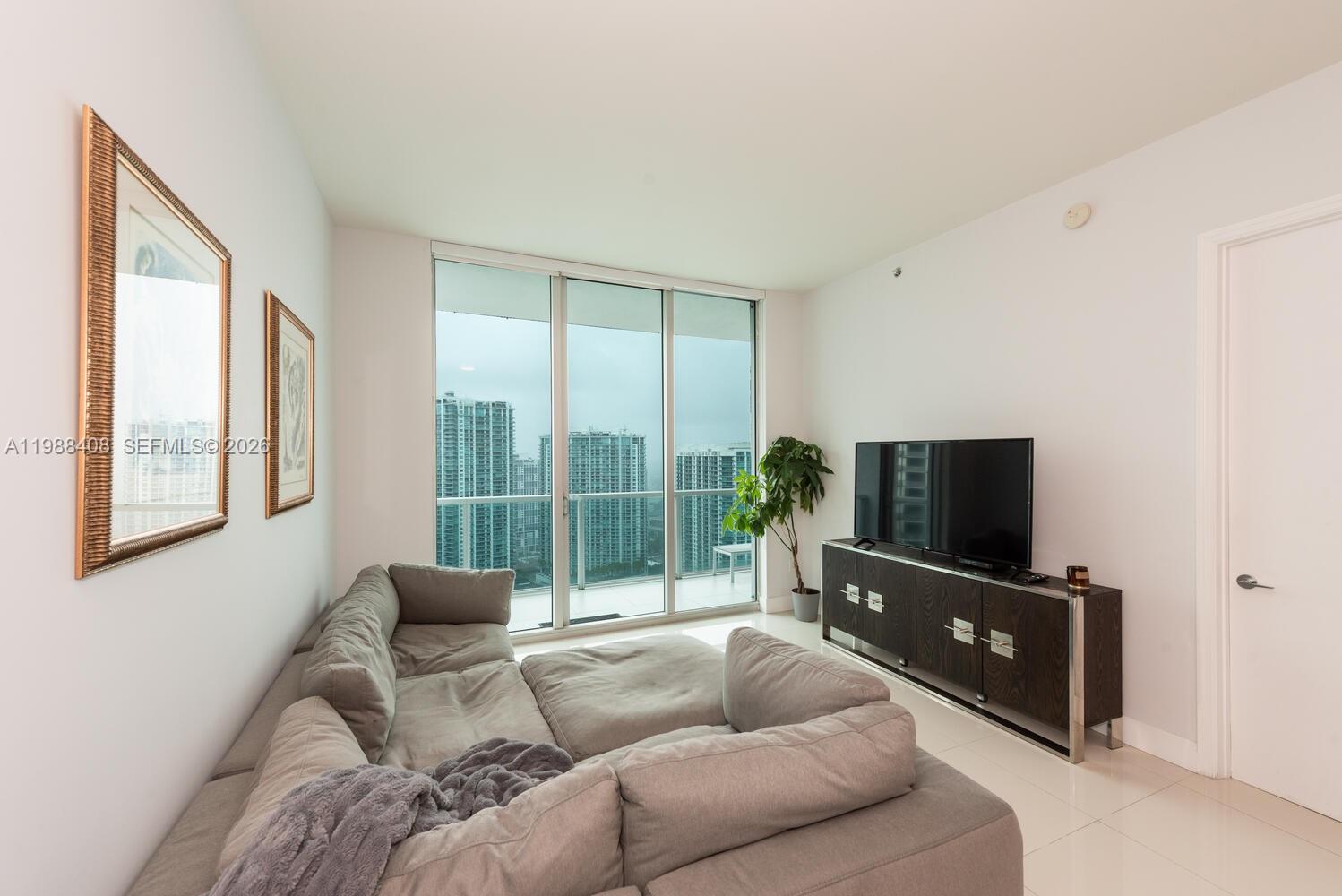 A living room features a grey sectional sofa, a television console, and floor-to-ceiling windows — 55 SE 6th St # 4200, Miami FL 33131, MIAMI, FL