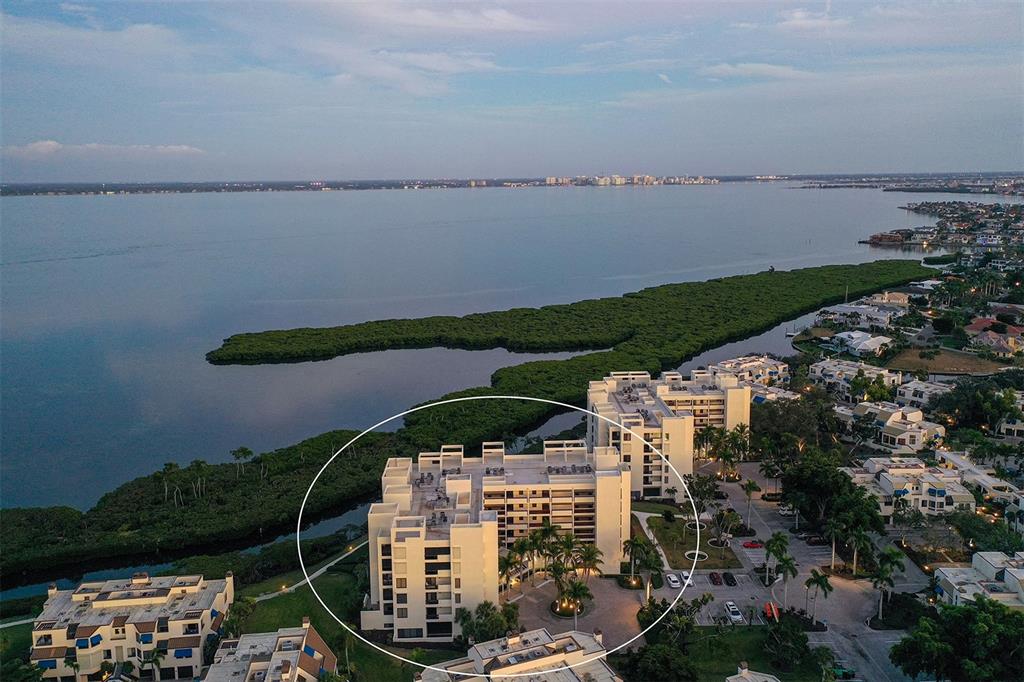 An aerial view shows a multi-story residential building surrounded by mangroves and a large bay — 1932 HARBOURSIDE DRIVE UNIT 242, LONGBOAT KEY, FL