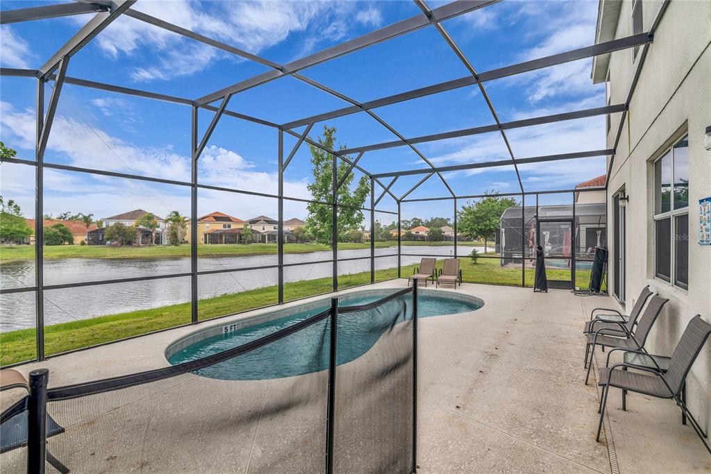 A screened-in patio features a small swimming pool, safety fence, and views of a lake — 2576 SHANTI DRIVE, KISSIMMEE, FL
