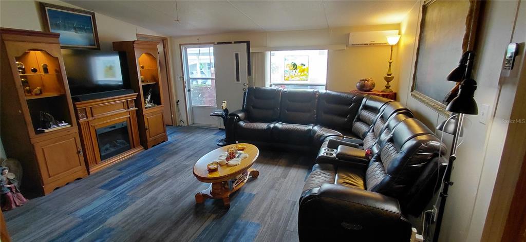 A living room features a dark leather sectional, a wooden fireplace console, and wood-look flooring — 221 HERON ROAD, CLEARWATER, FL