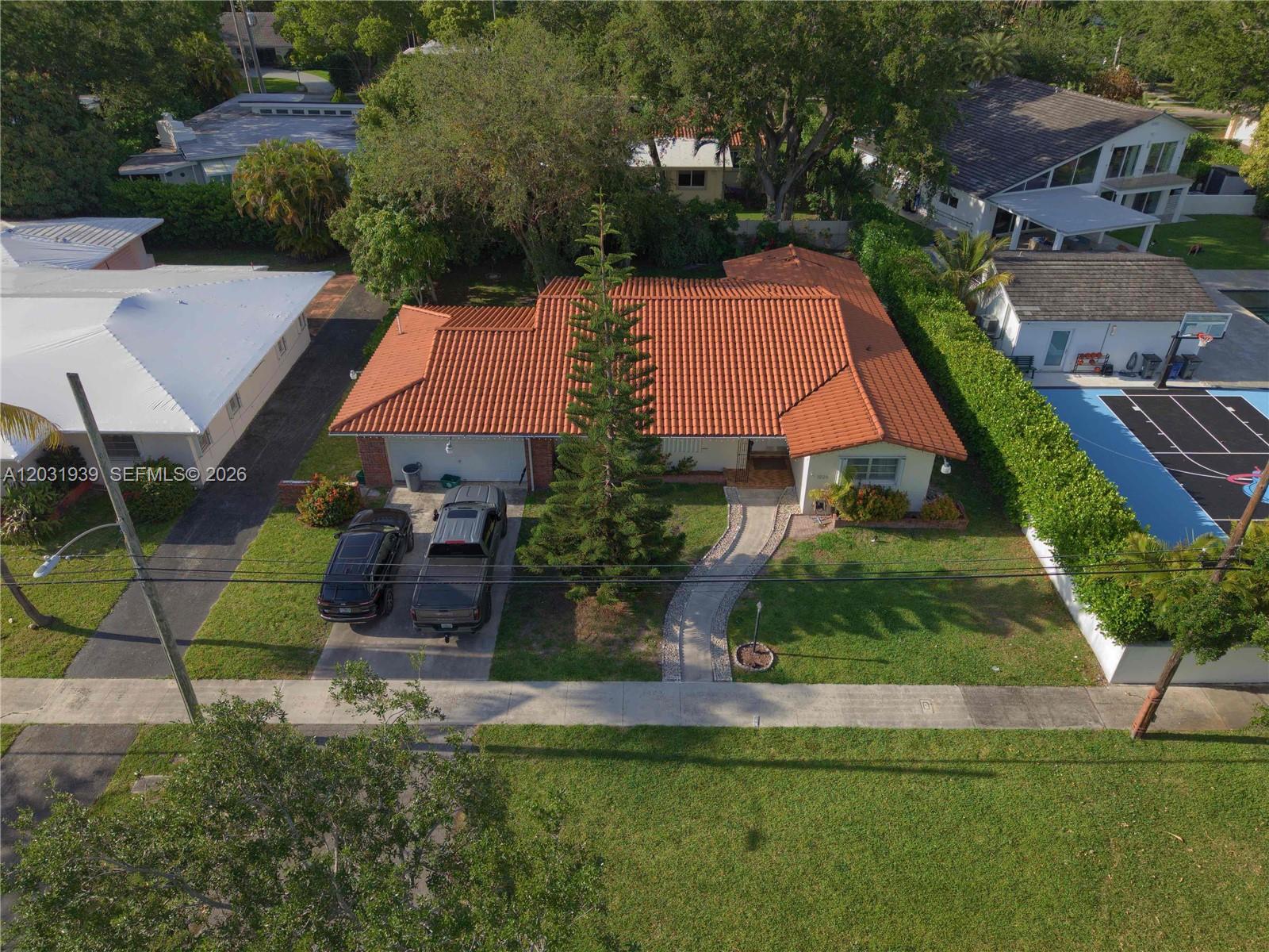 An aerial view shows a single-story house with a red tile roof and driveway — MIAMI SHORES, FL