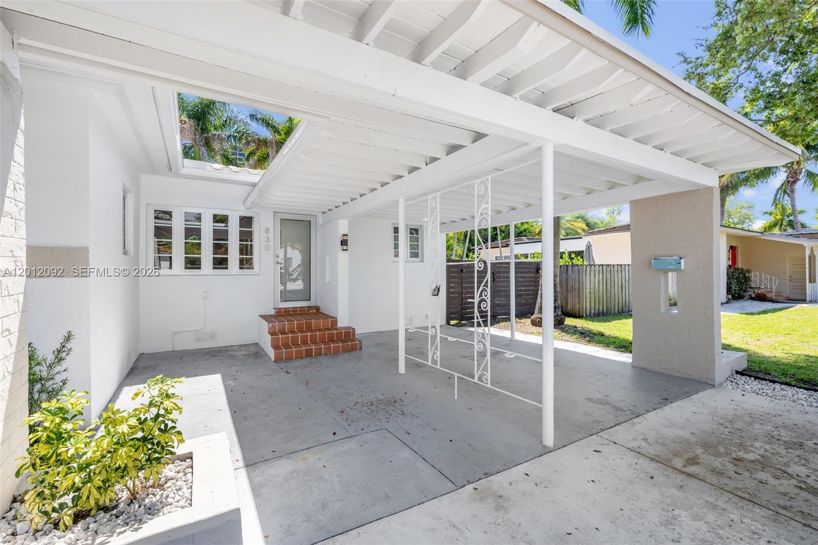 A white house exterior features a covered carport with decorative metal supports and brick steps — 830 NE 72nd St, Miami FL 33138, MIAMI, FL