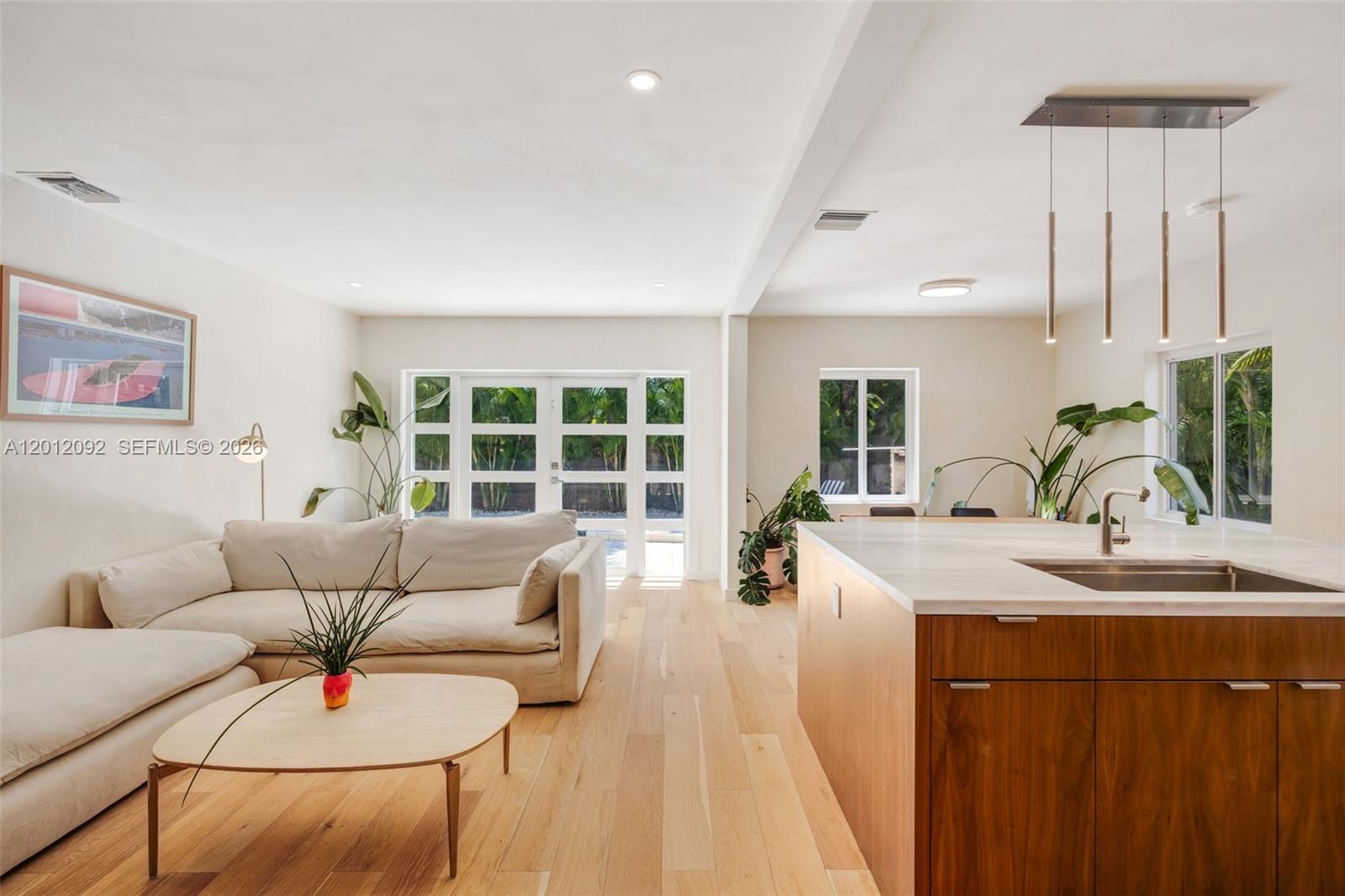 A living room and kitchen area feature light wood floors, a sofa, and a kitchen island — 830 NE 72nd St, Miami FL 33138, MIAMI, FL