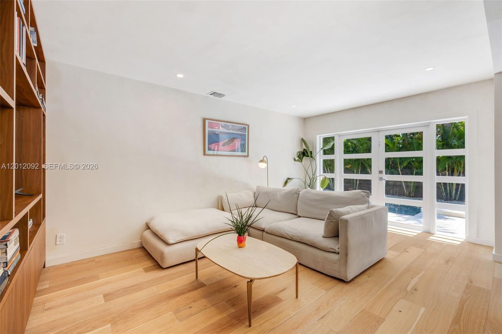 A living room features light wood flooring, a beige sectional sofa, and built-in wooden shelving — 830 NE 72nd St, Miami FL 33138, MIAMI, FL