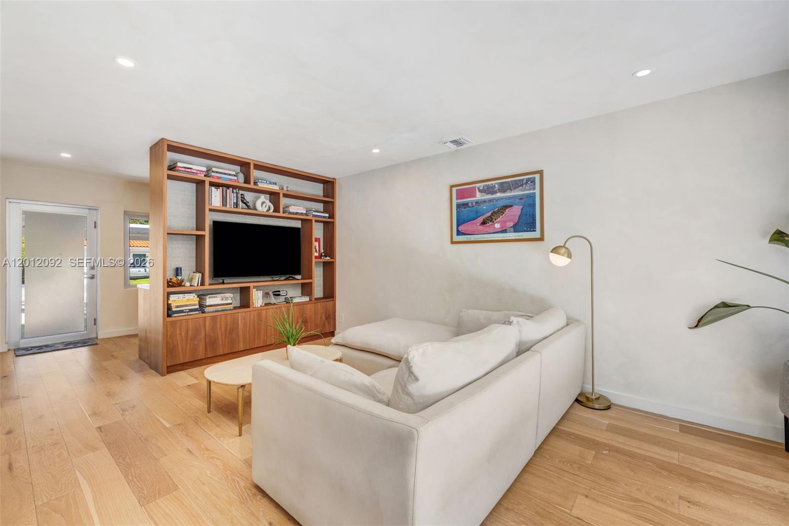 A living room features a wooden media shelving unit, a white sectional sofa, and hardwood floors — 830 NE 72nd St, Miami FL 33138, MIAMI, FL
