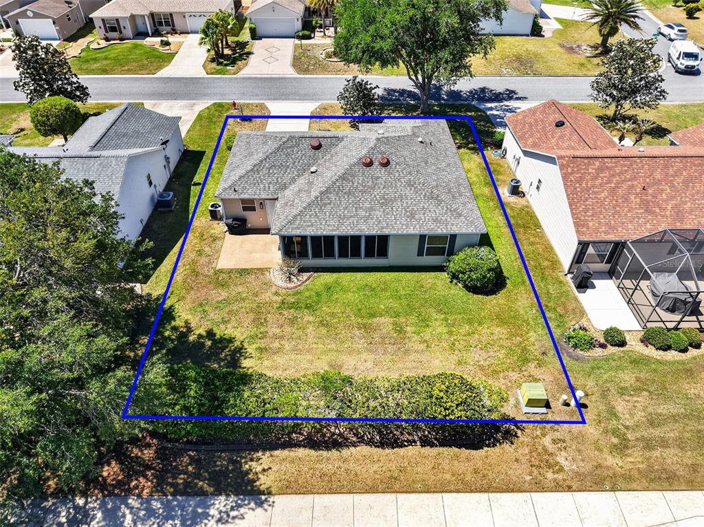 An aerial view shows the backyard and rear exterior of a single-story house with a patio — 1539 HOLLYBERRY PLACE, THE VILLAGES, FL