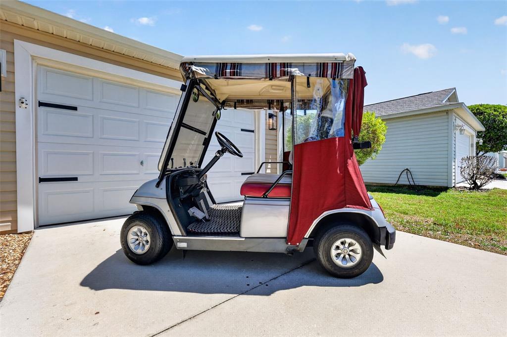 A silver golf cart with a red enclosure sits on a concrete driveway — 1539 HOLLYBERRY PLACE, THE VILLAGES, FL