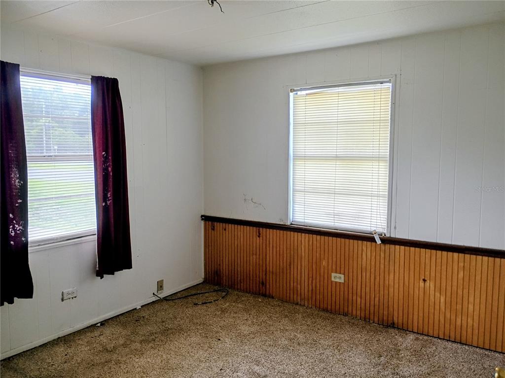 A bedroom features white paneled walls, wood wainscoting, carpeted flooring, and two windows with blinds — 4315 LAKE AVENUE, KISSIMMEE, FL