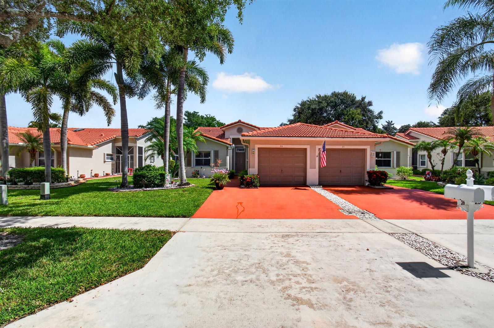 A single-story duplex with a red-tiled roof, two garage doors, and a red concrete driveway — 26 Sausalito Drive, Boynton Beach FL 33436, BOYNTON BEACH, FL