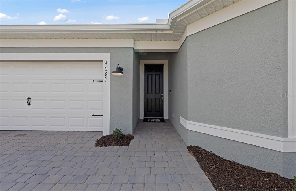 The exterior of a house features a gray stucco facade, a white garage door, and a walkway — 16335 LILLY ELAINE WAY, BRADENTON, FL