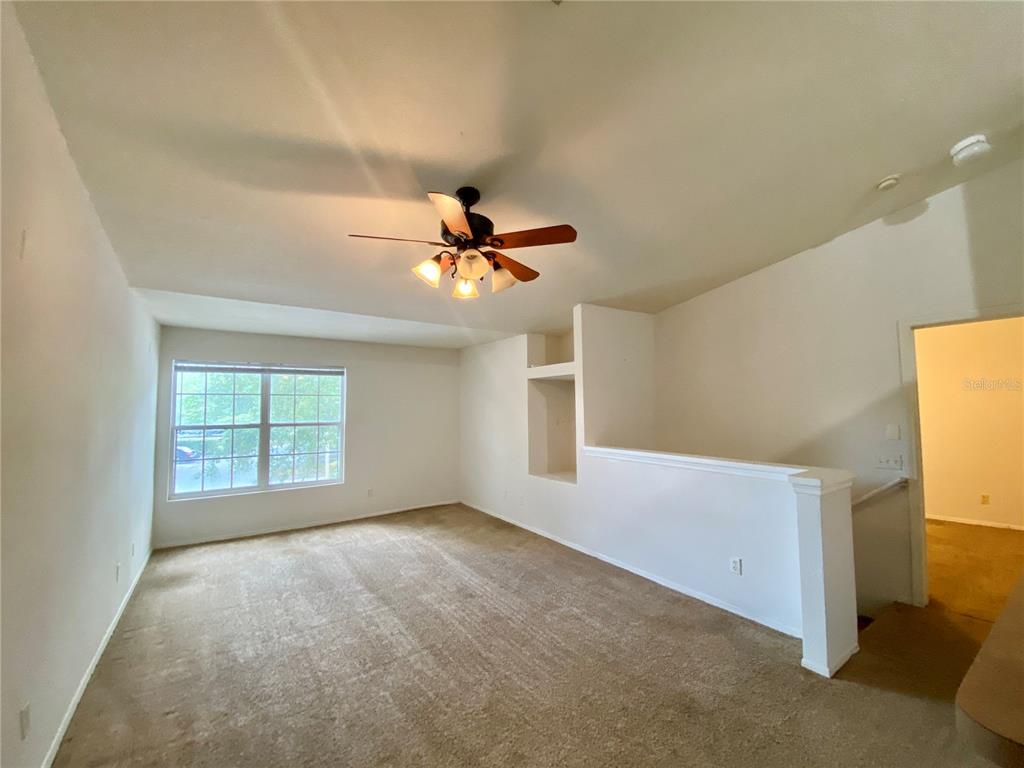 An empty living room features beige carpeting, a ceiling fan, and a built-in wall niche — 36101 DEER CREEK DRIVE UNIT 202, ZEPHYRHILLS, FL