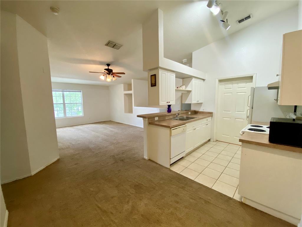 An open-concept kitchen with white cabinets and a breakfast bar overlooks a carpeted living area — 36101 DEER CREEK DRIVE UNIT 202, ZEPHYRHILLS, FL