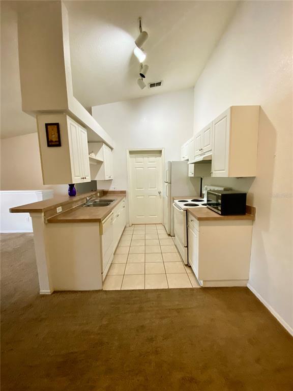 A kitchen with white cabinets, laminate countertops, tile flooring, and a white refrigerator — 36101 DEER CREEK DRIVE UNIT 202, ZEPHYRHILLS, FL