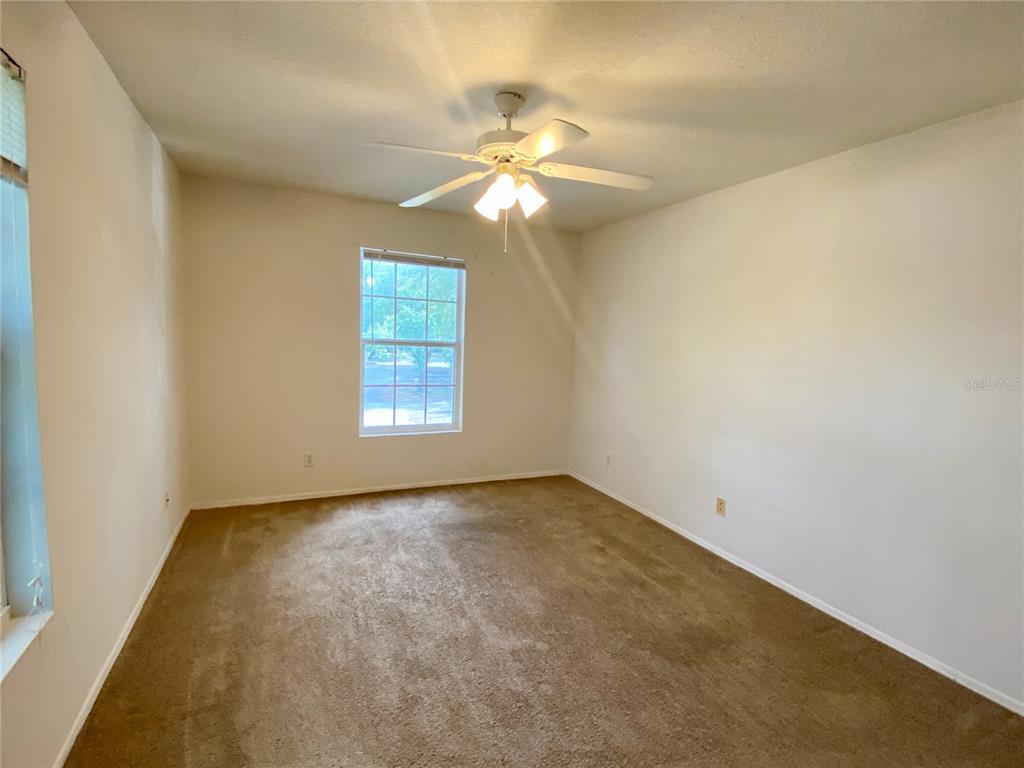 An empty bedroom with beige carpet, white walls, a ceiling fan, and a single window — 36101 DEER CREEK DRIVE UNIT 202, ZEPHYRHILLS, FL