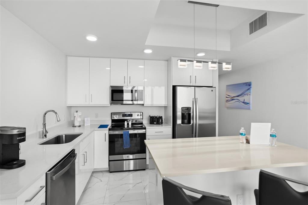 A modern kitchen features white cabinets, stainless steel appliances, and a large central island — 11500 GULF BOULEVARD UNIT 202, ST PETERSBURG, FL